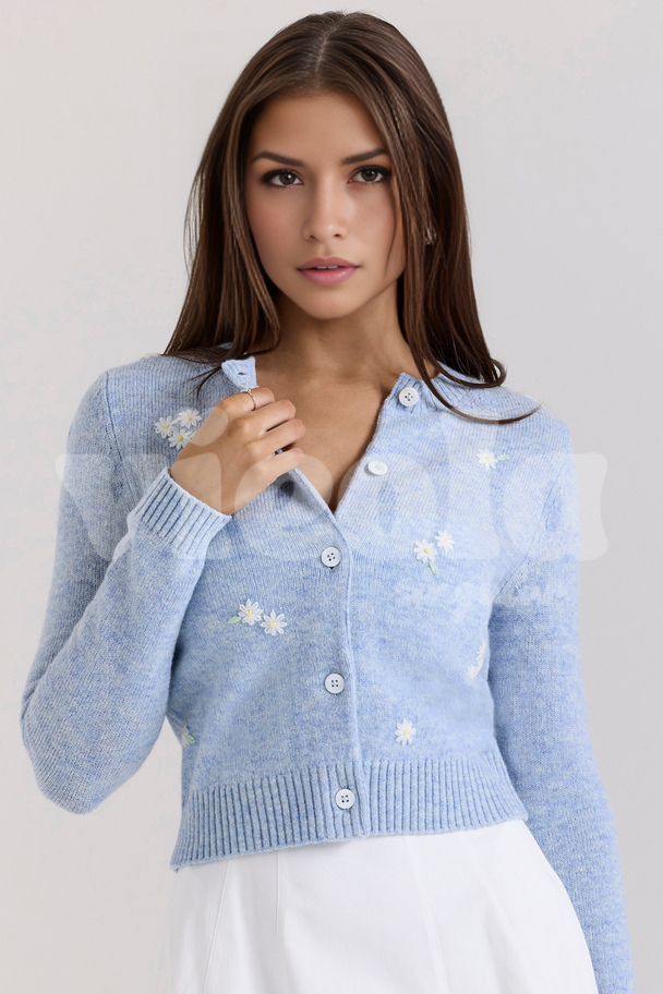 Woman wearing a light blue cardigan with white floral patterns on a plain background