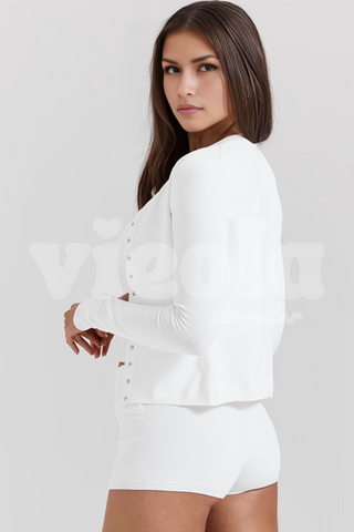 Woman wearing a white long-sleeve top and shorts on a plain background