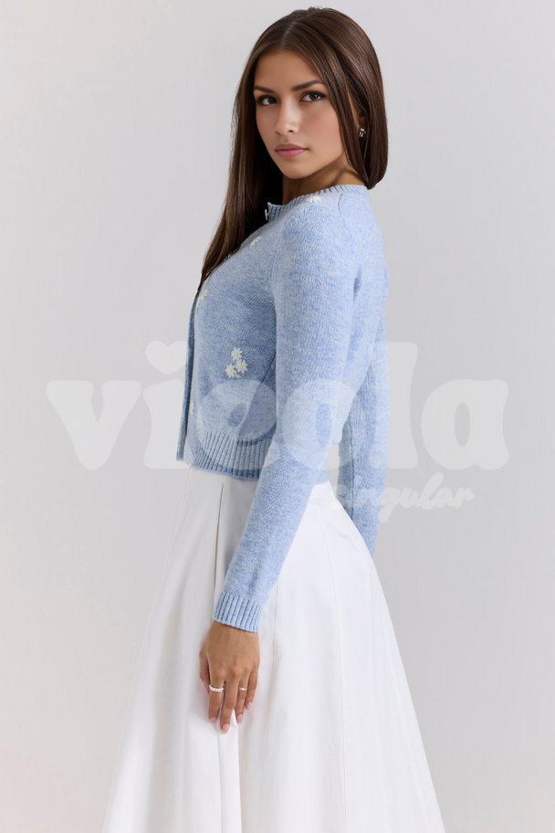Woman wearing a light blue knitted cardigan over a white dress on a plain background
