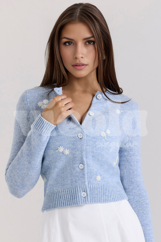 Woman wearing a light blue cardigan with white floral patterns on a plain background