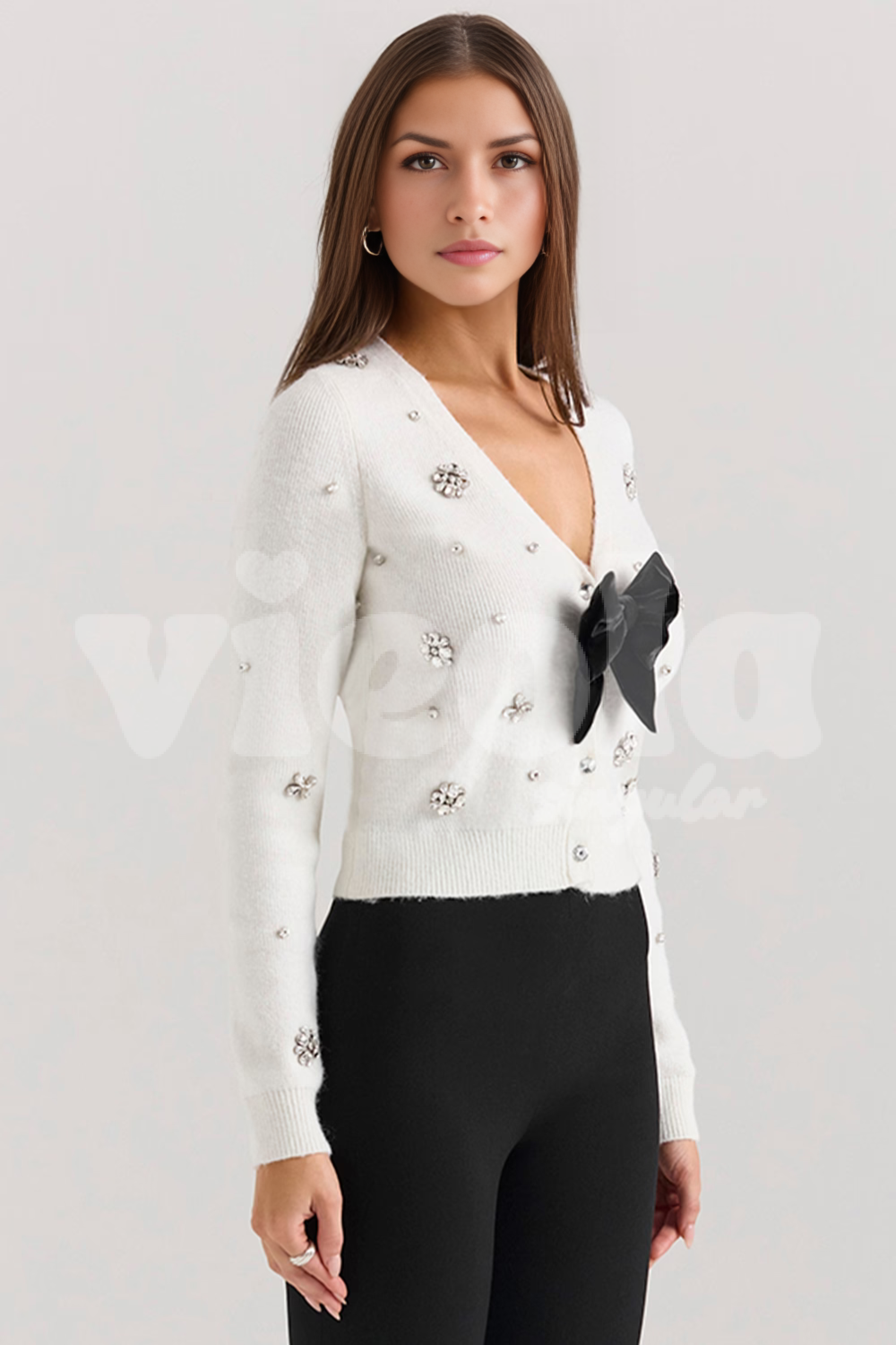 Woman wearing a white embellished cardigan with a black bow on a light gray background