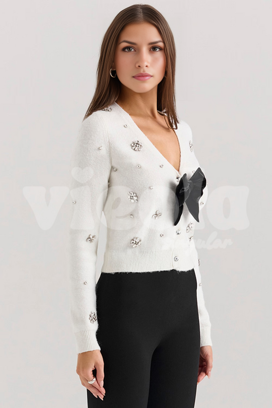 Woman wearing a white embellished cardigan with a black bow on a light gray background